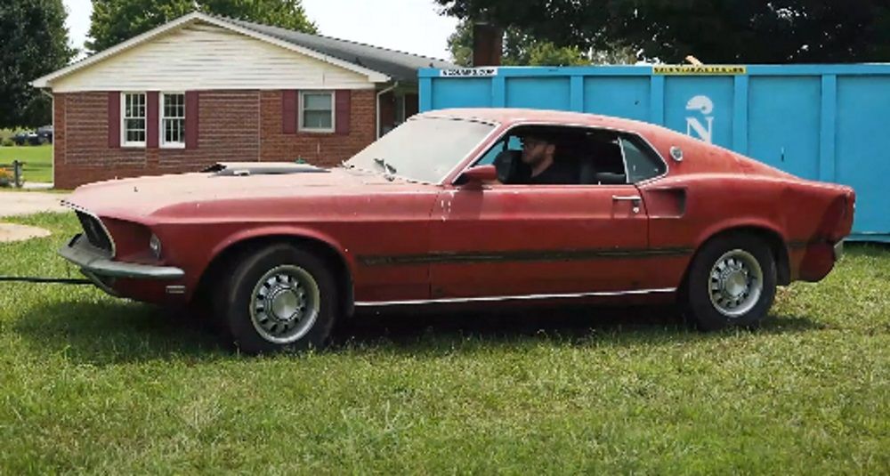 A 1969 M-Code Ford Mustang Fastback being towed on grass, red, side profile